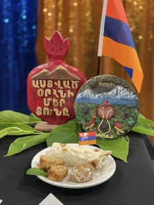 A plate of Armenian food sits in front of decorative items, including a small Armenian flag, a plate with "Armenia" written on it, and a red ornament with Armenian script—celebrating Armenian culture and heritage.