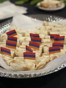 A platter of rolled flatbread wraps, each topped with a toothpick flag in red, blue, and orange stripes—perfect for celebrating Armenian Heritage Month and honoring Armenian heritage.