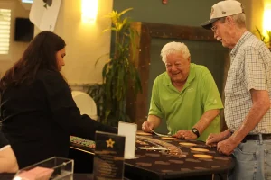 Two older men play blackjack at a casino table while a female dealer manages the game during Casino Night.