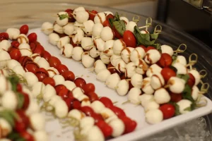 Skewers of cherry tomatoes, mozzarella balls, and basil leaves are arranged on a white tray, drizzled with balsamic glaze—perfect bite-sized treats for your Casino Night spread.
