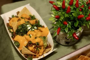 A tray of nachos topped with ground meat, melted cheese, and chopped cilantro sits next to a small potted plant with red chili peppers, perfect for a festive Cinco de Mayo celebration.