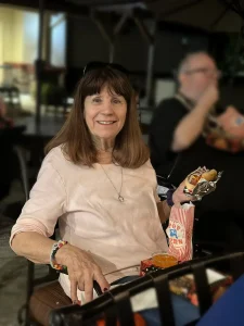 A woman sits smiling at Cinema Under the Sky, holding a hot dog in one hand and a bag of popcorn in the other, with more food and people in the background.