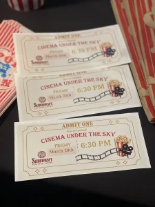 Three "Cinema Under the Sky" outdoor cinema event tickets for Friday, March 20th at 6:30 PM from Summerset Assisted Living, with popcorn and film reel graphics.