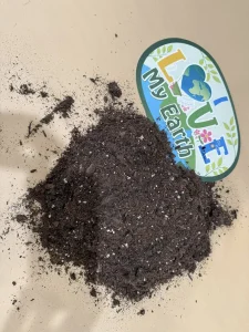 A pile of soil is spread on a flat surface next to a sign that reads "LOVE My Earth" with a heart and Earth graphic.