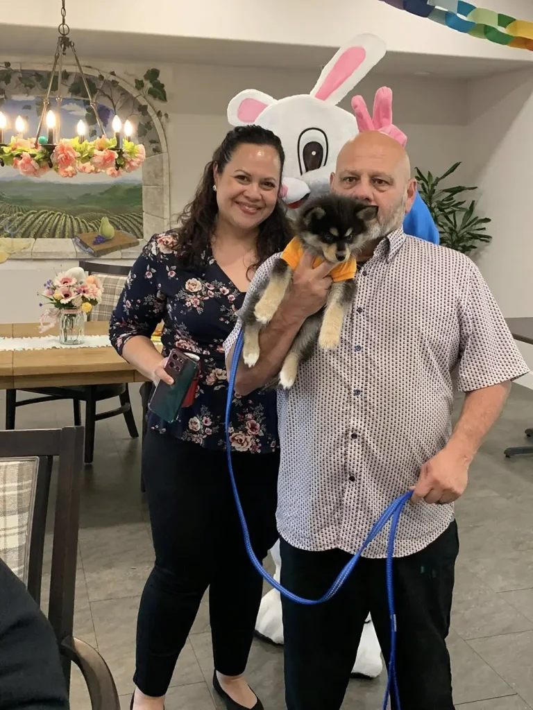 A man and woman pose with a small dog on a leash as the Easter Bunny stands behind them in a decorated indoor setting, capturing the joy of festive Easter activities.