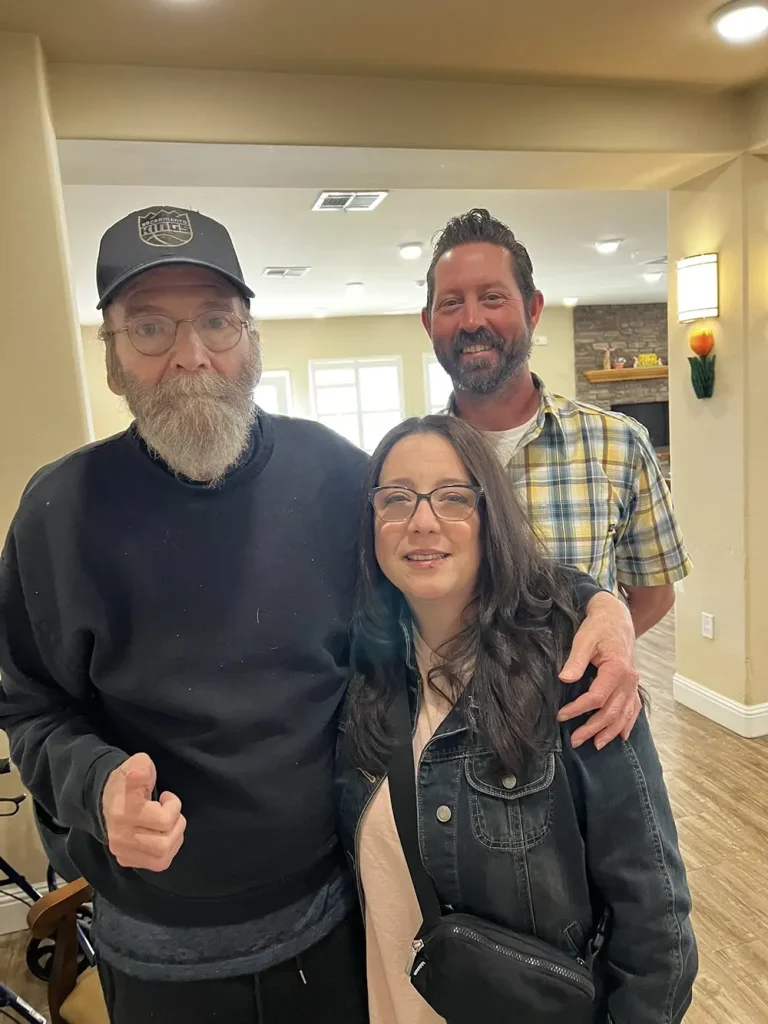 Three adults pose together indoors, perhaps after enjoying some Easter activities; the man on the left wears a black cap and sweatshirt, the man in back sports a plaid shirt, and the woman in front wears glasses and a black jacket.