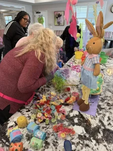 People gather around a kitchen island decorated with artificial flowers, ribbons, and an Easter bunny figure, enjoying Easter activities and working on crafts together.
