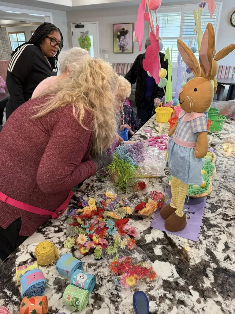 People gather around a kitchen island decorated with artificial flowers, ribbons, and an Easter bunny figure, enjoying Easter activities and working on crafts together.