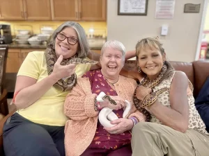 Three women sit on a couch smiling; the two on the ends each have a snake around their neck, while the woman in the center holds a white snake—capturing an unforgettable moment from their Exotic Animal Safari adventure.