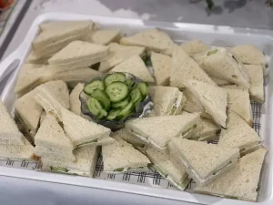 A tray of cucumber sandwiches with crustless white bread, arranged around a small bowl of sliced cucumbers—perfect for a gathering celebrating International Women’s Day and the spirit of women empowerment.