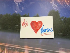 A note reads "We ♥ Nurses" in red and blue marker, taped to a surface with a blurred outdoor background—perfect as heartfelt Nurse Appreciation Cards.