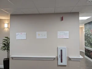 Three hand-drawn Nurse Appreciation Cards are taped to a beige hallway wall above a fire extinguisher box and next to a potted plant.