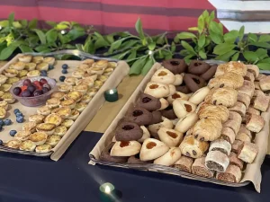 Two trays of assorted pastries and cookies are displayed on a table, with small candles and green leafy decorations in the background, creating a festive Jubilee atmosphere reminiscent of Queen Esther’s celebrations.
